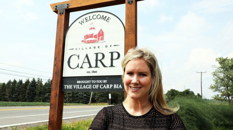 A photo of a person standing in front of a Vilalge of Carp sign.