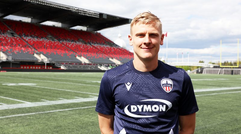 A soccer player poses for a photo inside a stadium.