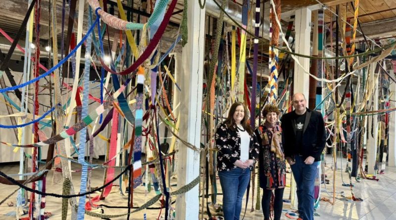 Three people pose beside an installation.