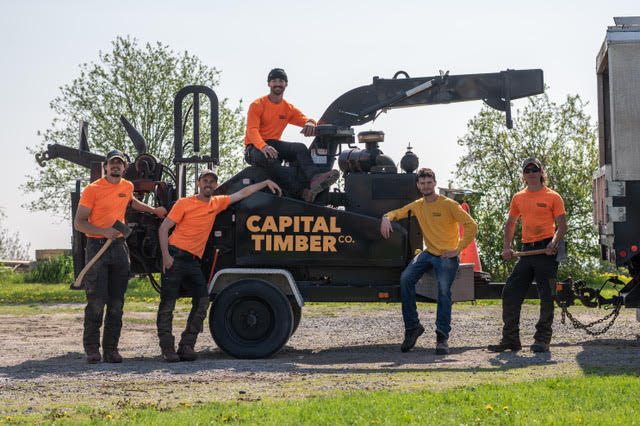 A group of people pose around a wood chipper.