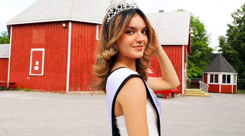 A person in a tiara poses in front of a barn.