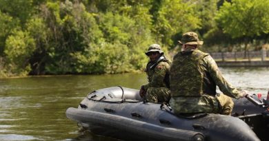 Two soldiers operate a small rubber boat.