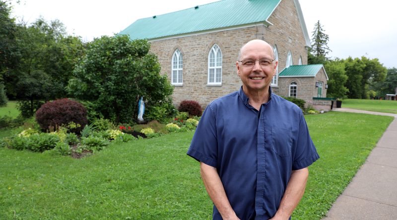 A priest poses in front of a church.