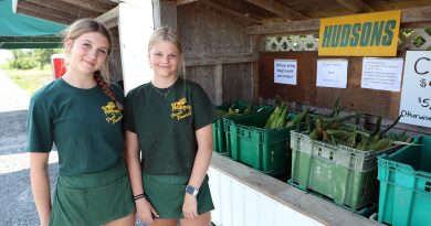 Two people pose before a vegetable stand.