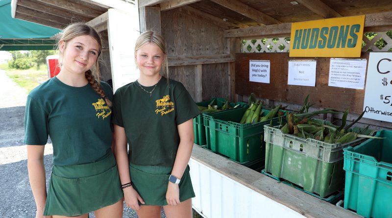 Two people pose before a vegetable stand.