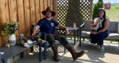 Two people pose on a porch with cats.