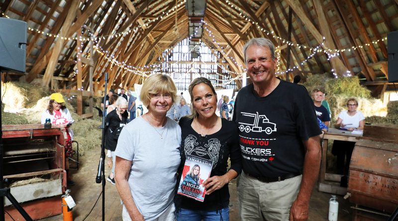 Three poeple pose in a barn.