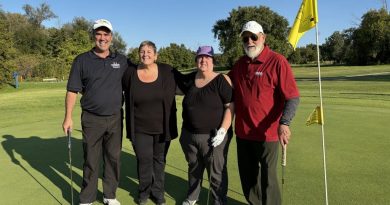 Four people pose for a photo on a golf course.