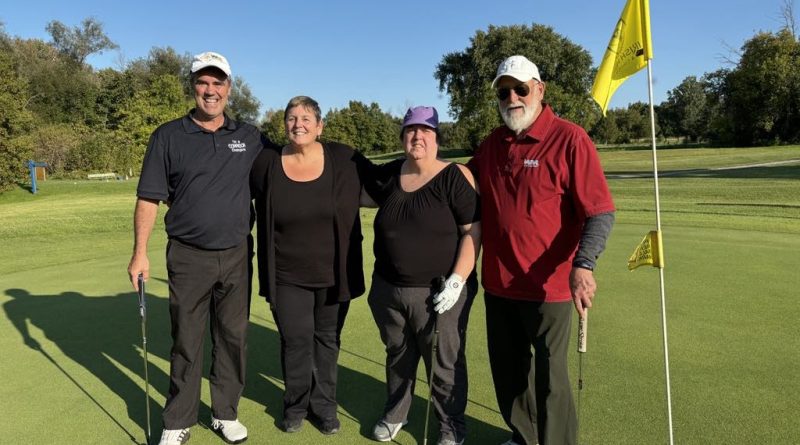 Four people pose for a photo on a golf course.