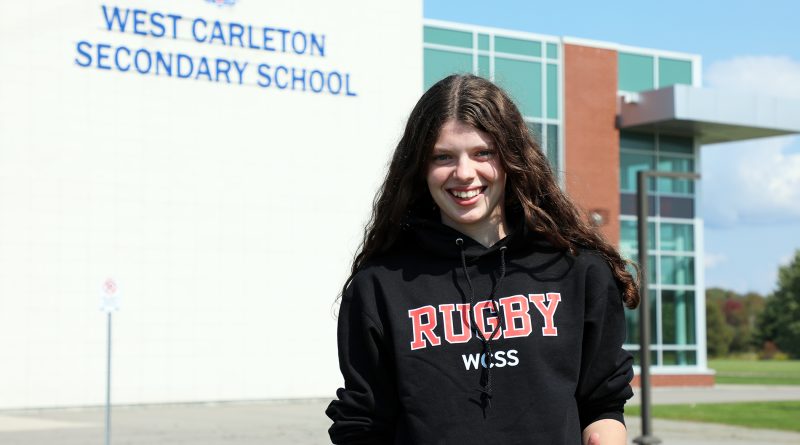 A person poses in front of a school.