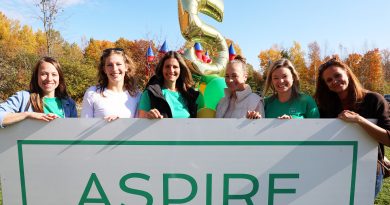 Six people pose behind a sign.