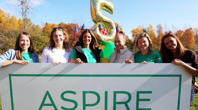 Six people pose behind a sign.