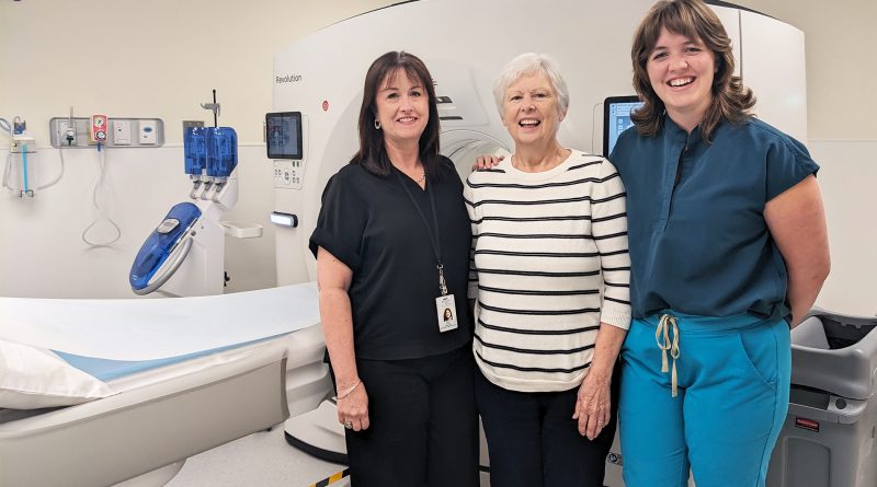 Three people pose in front of a scanner.