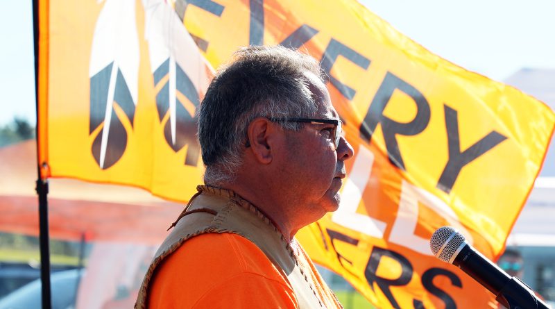 A man speaks in front of a flag.