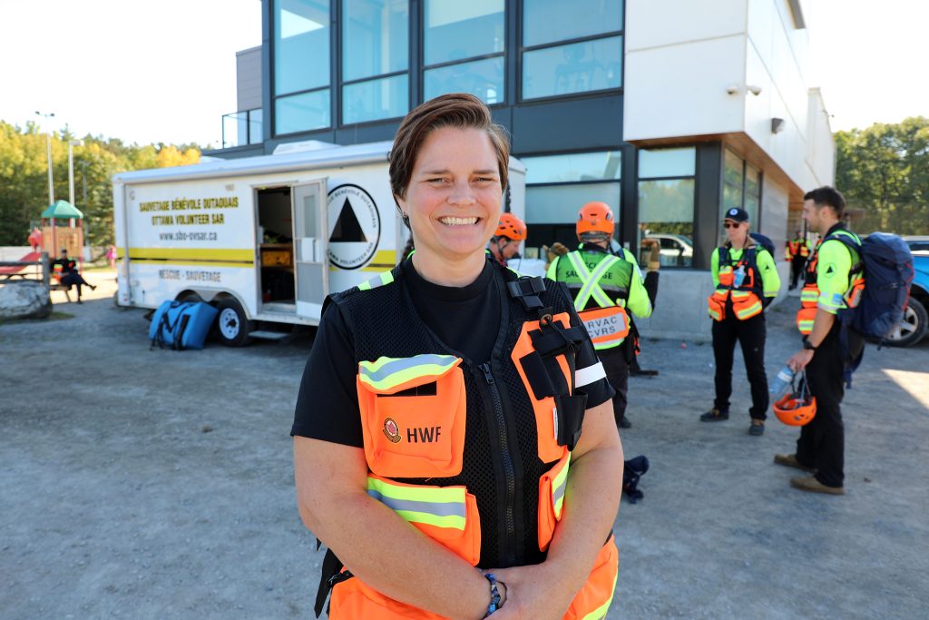 A woman poses in front of volunteer search and rescue personnel. Photo by Jake Davies