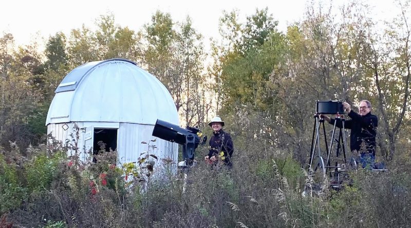 Two people pose beside their telescopes.