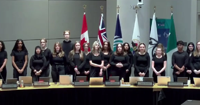 A choir sings in a council chamber.