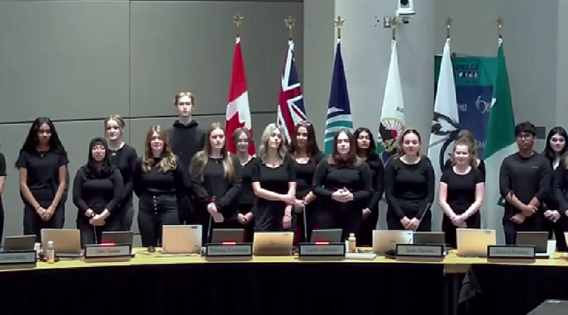 A choir sings in a council chamber.