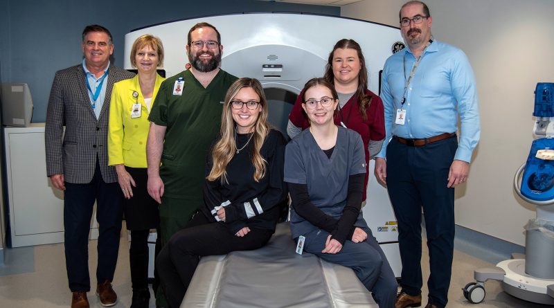 A group poses around a CT scanner.