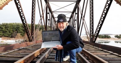 A man stands on a train bridge with a computer.