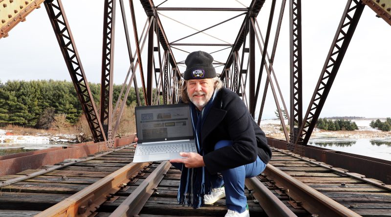 A man stands on a train bridge with a computer.