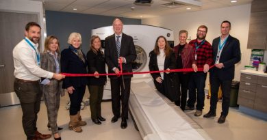 People cut a ribbon in front of a CT scanner.