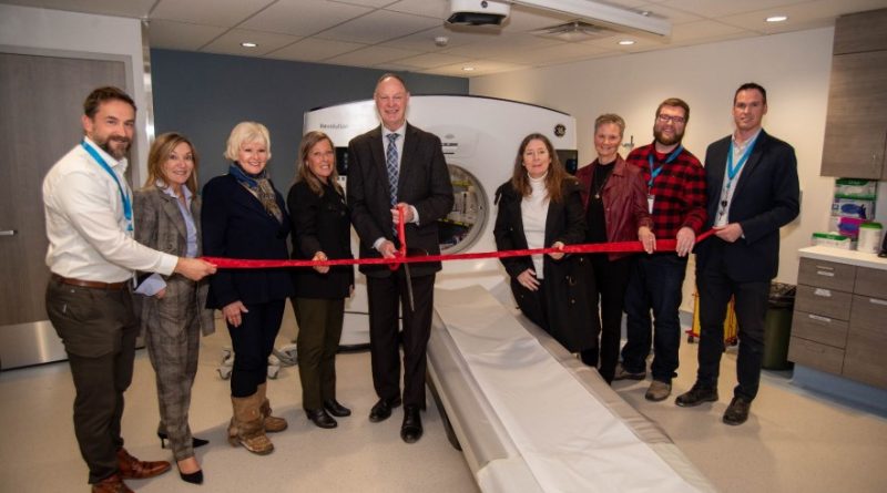 People cut a ribbon in front of a CT scanner.