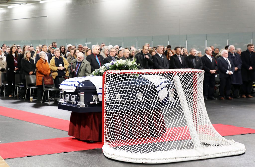 A casket stands in front of a hockey net during a funeral.