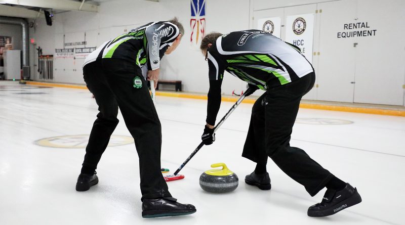 Two people sweep a curling stone.