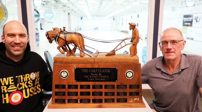 Two people pose beside a trophy.