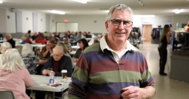 A man poses in a room full of euchre players.