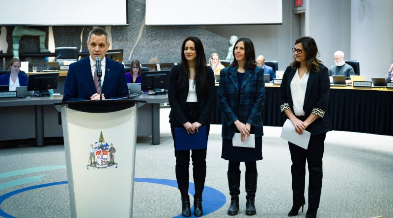 Four people stand at a podium at city hall.