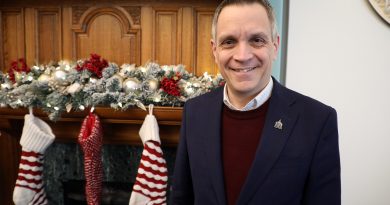 A mayor poses in front of a fireplace.