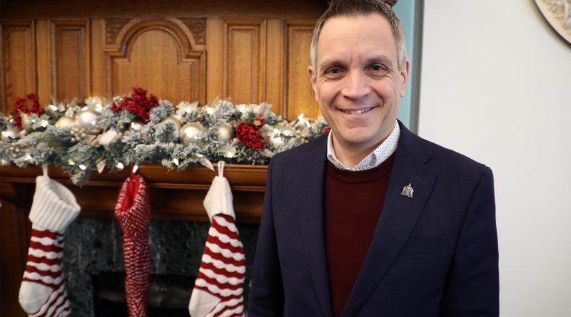 A mayor poses in front of a fireplace.