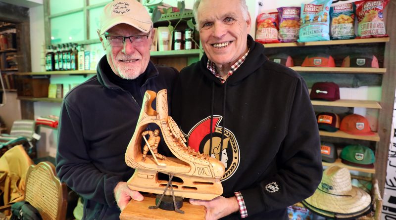 Two people pose with a wood carving of a skate.