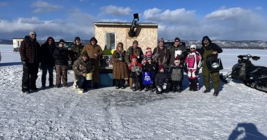 Ice anglers pose in front of an ice shack.