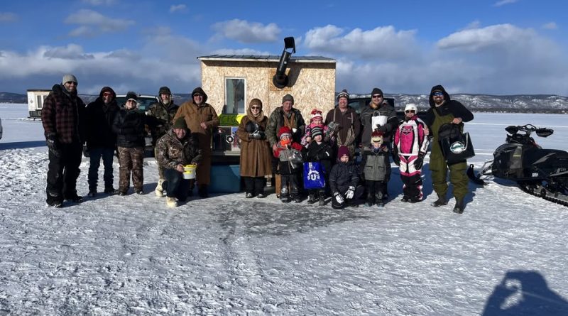 Ice anglers pose in front of an ice shack.