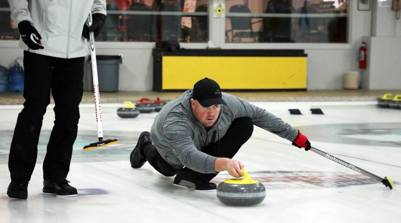 A man delivers a stone during a curling match.