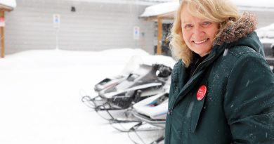 A woman poses in front of some snowmobiles.