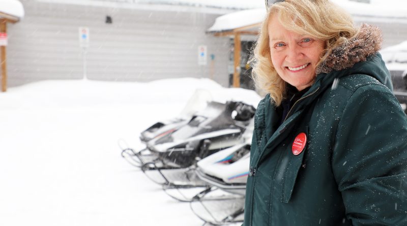 A woman poses in front of some snowmobiles.