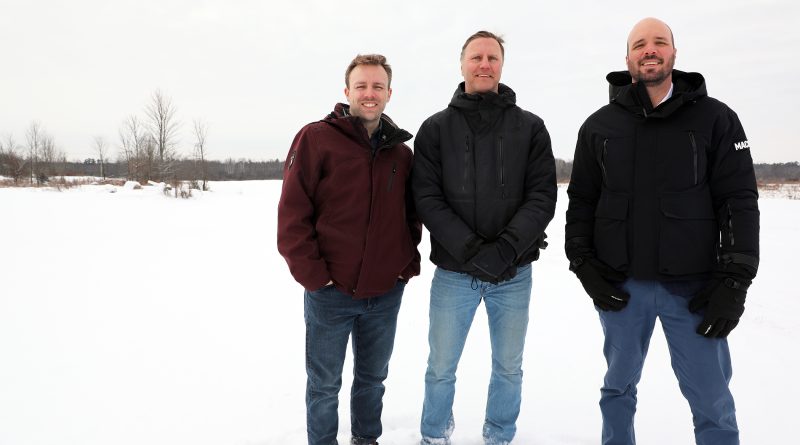 Three people pose in a snowy field.