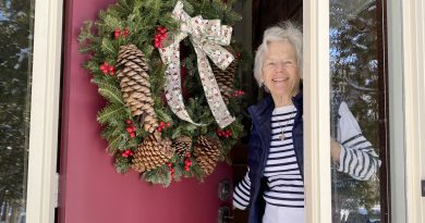 A woman smiles from her door.