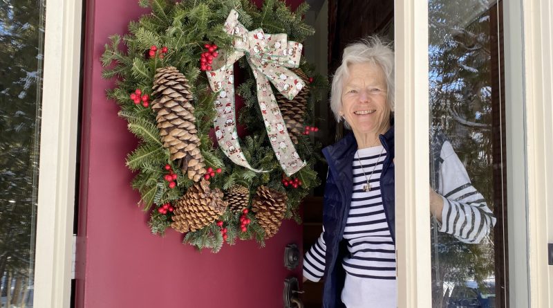 A woman smiles from her door.