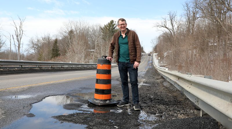 A man stands by a pothole.