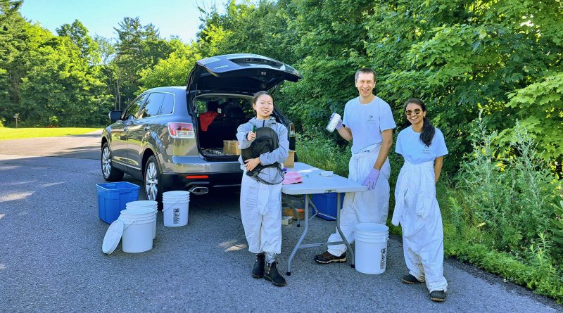 Three people do science work behind a car.