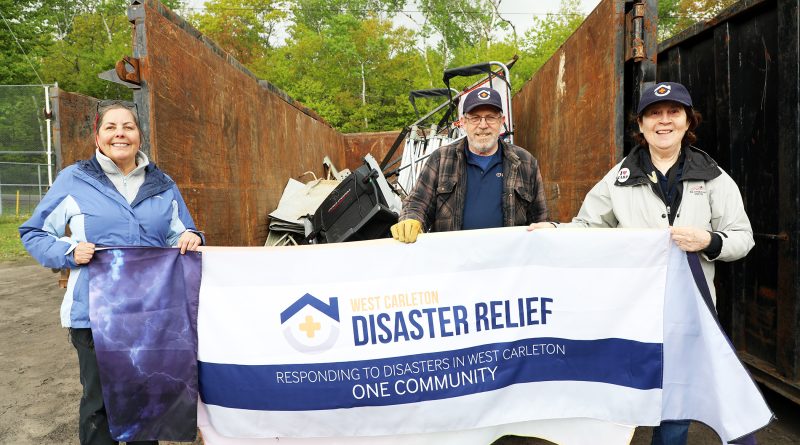 Three people hold a banner in front of a dumpster.