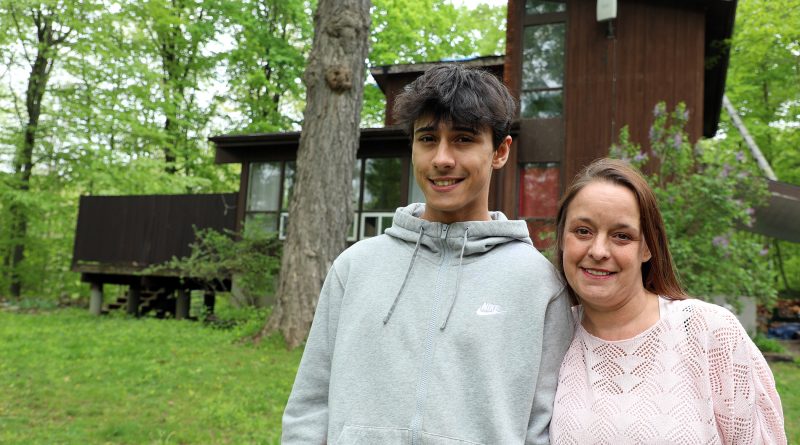 Two people pose in front of a house.