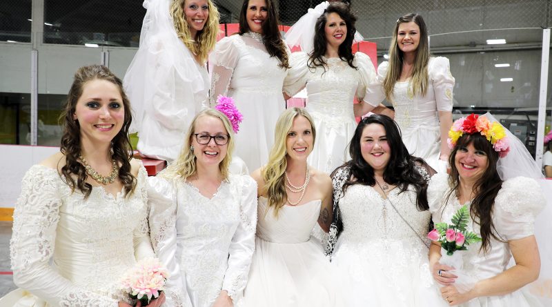 A group of women in wedding dresses pose for a photo.