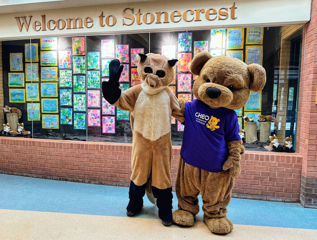 A bear stands beside a fox inside a school.