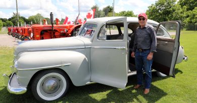A man poses in front of a classic car.